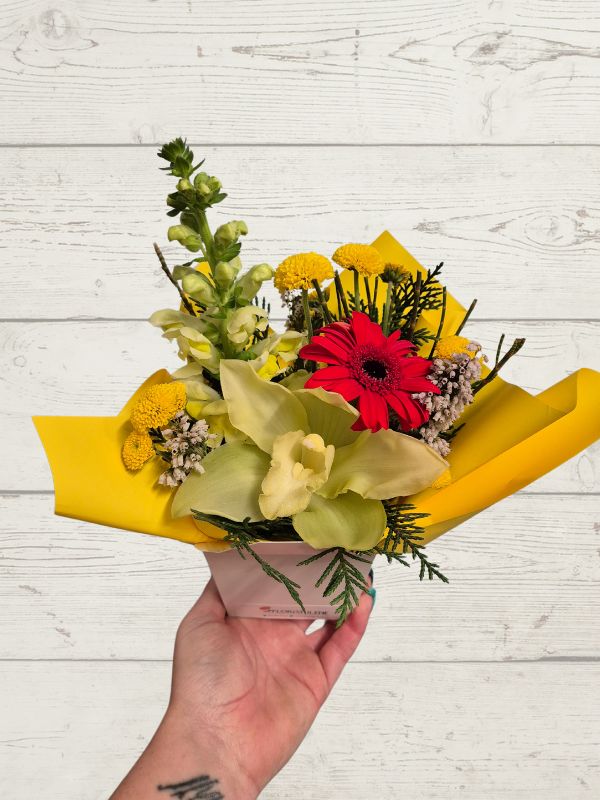 Bouquet of flowers with yellow and red flowers in a hand against a light wooden background