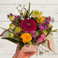 Bouquet of colorful flowers held by a hand on a light wooden surface