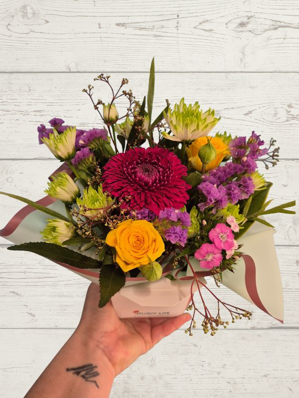 Bouquet of colorful flowers held by a hand on a light wooden surface
