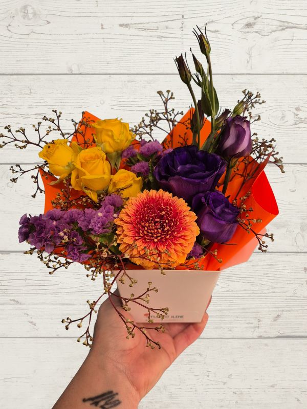 Colorful bouquet of flowers held by a hand on a light wooden background