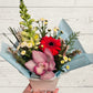 Bouquet of flowers with pink orchids and red gerbera daisies held against a light wooden background