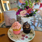 A fresh flower posy with two cupcakes and a handmade card displayed on a table.