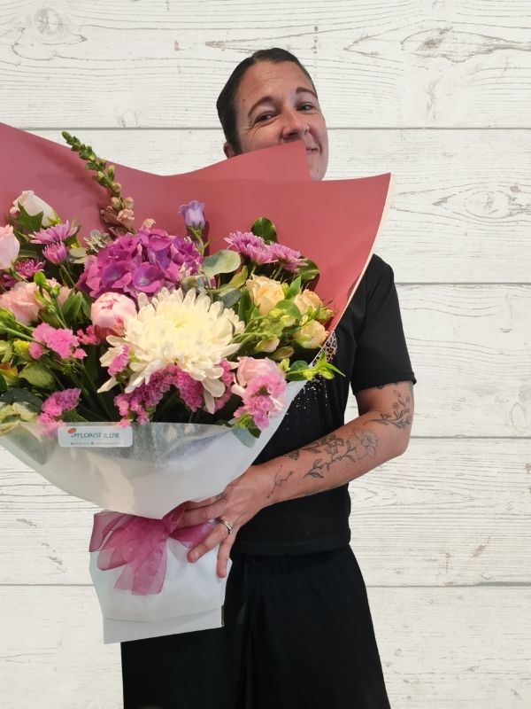 a person holding a bouquet of flowers in pink and white wrapped in pink and white paper.
