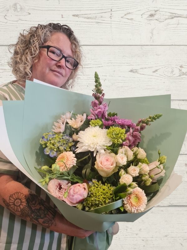 person holding a bouquet of fresh flowers in pink, white and mauve in a green and white wrap. 