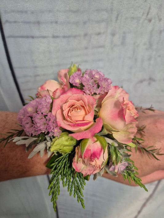 A wrist corsage featuring pink and purple flowers attached to a pink organza ribbon.