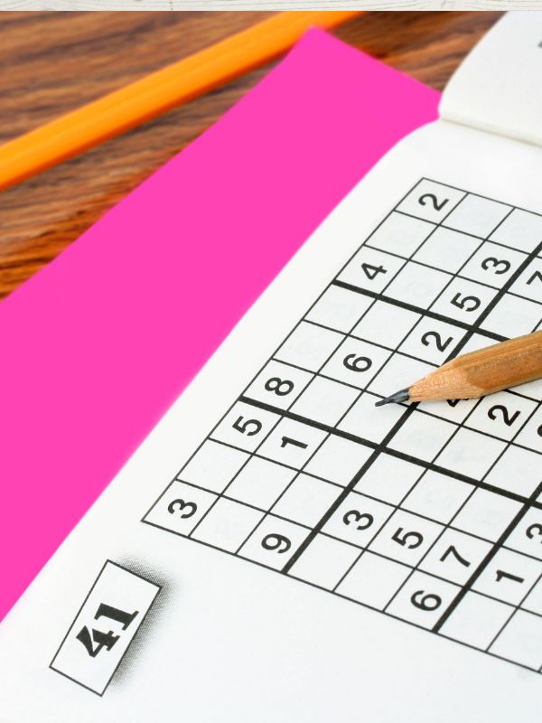 A puzzle book with a pen on top, featuring a grid of numbers and a pink eraser behind it.