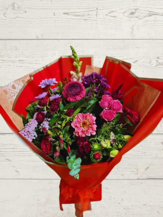 A bouquet of fresh flowers in red and pink shades, wrapped in a red paper.