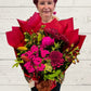 A person holding a red palette bouquet of various flowers, with a focus on the red and pink flowers.