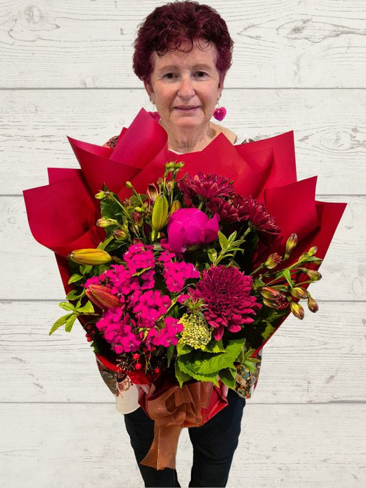 A person holding a red palette bouquet of various flowers, with a focus on the red and pink flowers.