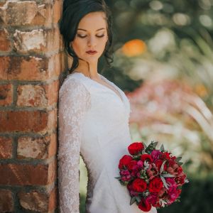 bride holding red wedding posy leaning against a brick wall