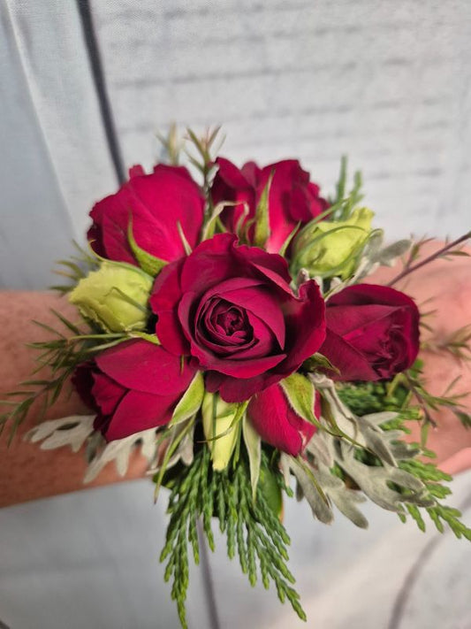 A red wrist corsage made of flowers, attached to a red organza ribbon.