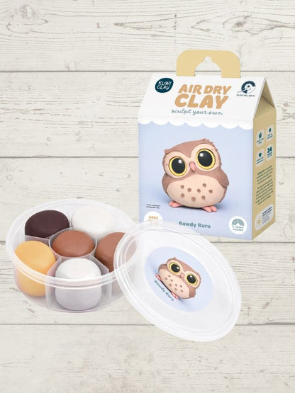 Rowdy Ruru Air Dry Clay sculpting kit featuring a box with an owl illustration and a clear plastic container of colorful clay balls, displayed on a light wood background.