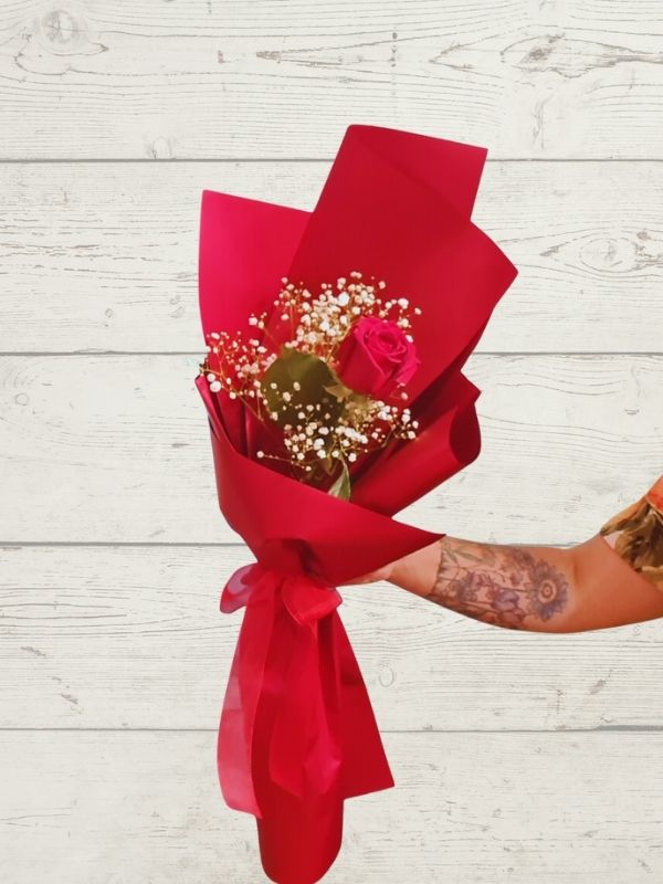 single red rose with white greenery gift wrapped in red paper with a red bow