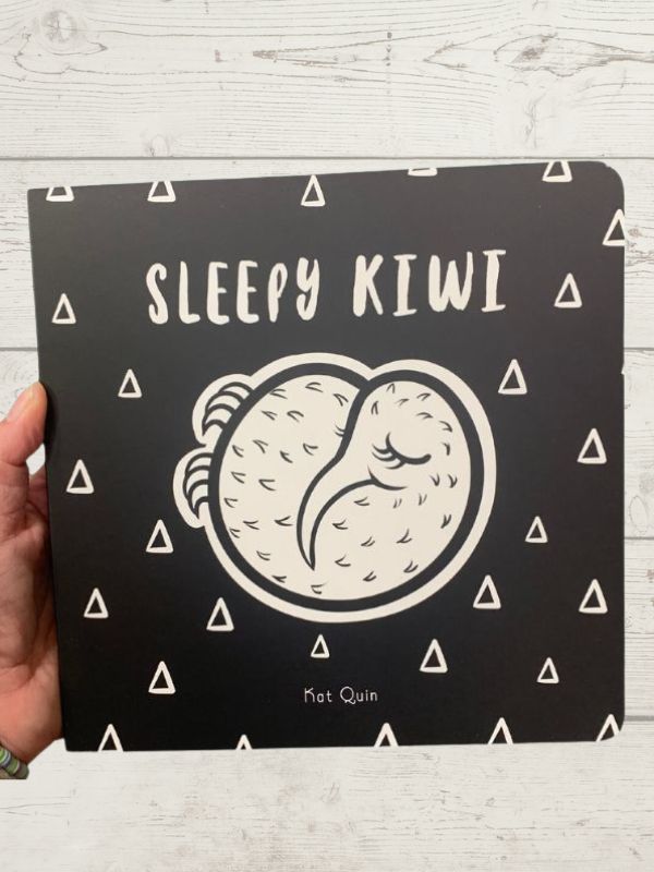 A book cover for 'Sleepy Kiwi' with a black and white design featuring an illustration of a kiwi bird and triangular patterns.