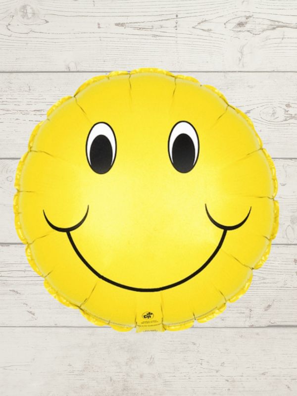 A smiley face balloon with a yellow color and a happy facial expression, placed against a wooden background.