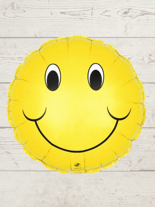 A smiley face balloon with a yellow color and a happy facial expression, placed against a wooden background.