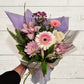Bouquet of flowers with purple and white paper wrap on a light wooden surface