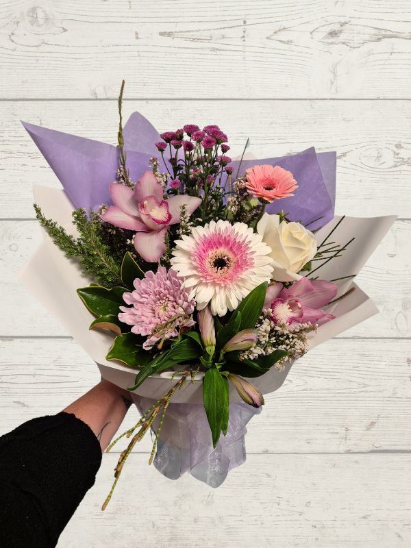 Bouquet of flowers with purple and white paper wrap on a light wooden surface