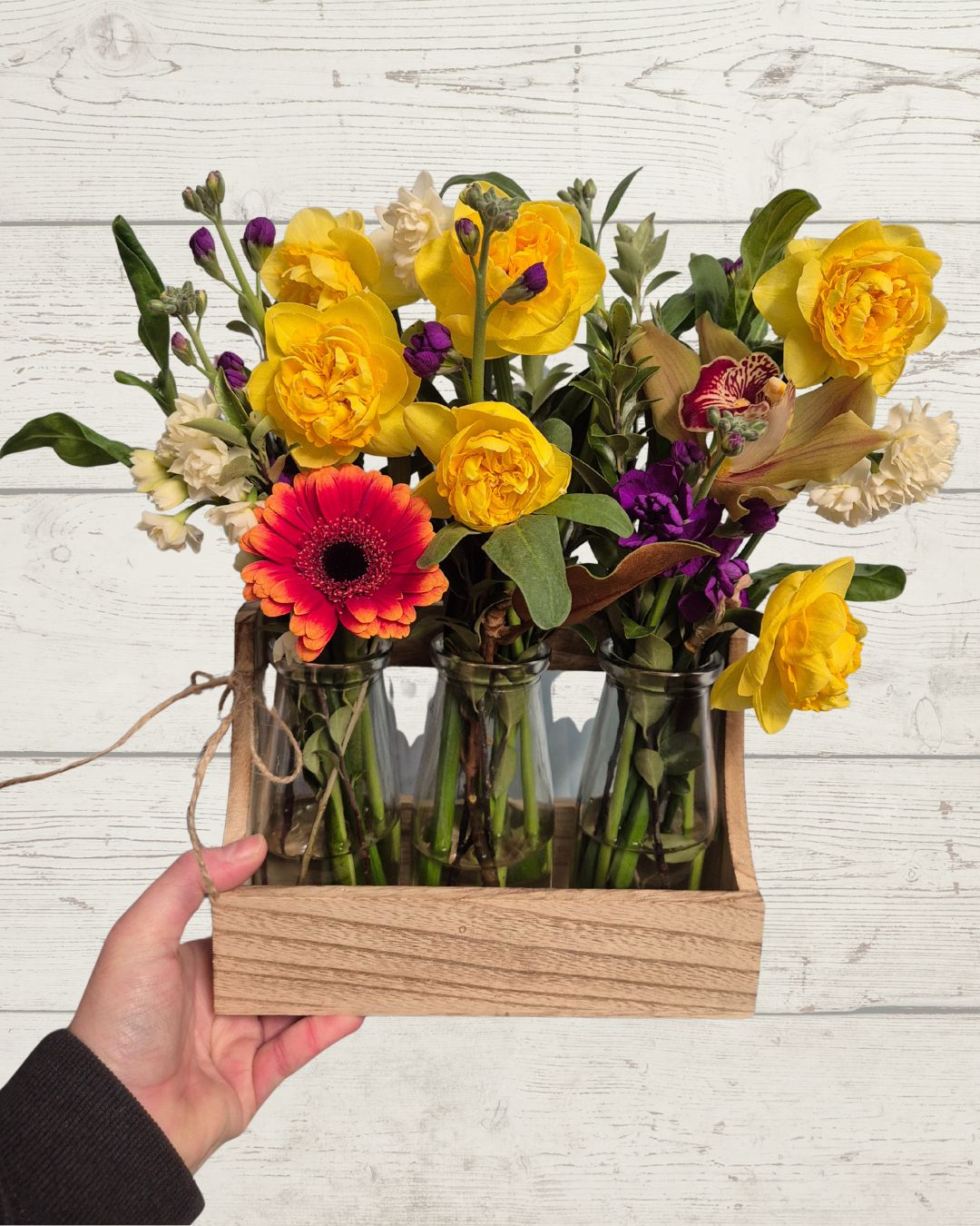 Hand holding a wooden box with colorful flowers against a light wooden background