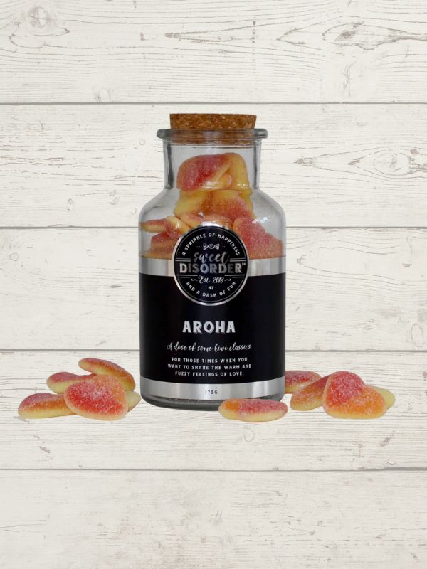 Bottle labeled 'Aroha' with gummy candies on a wooden surface