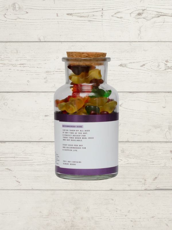 Glass jar with cork lid filled with colorful gummy bears on a light wooden surface