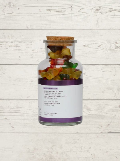 Glass jar with cork lid filled with colorful gummy bears on a light wooden surface