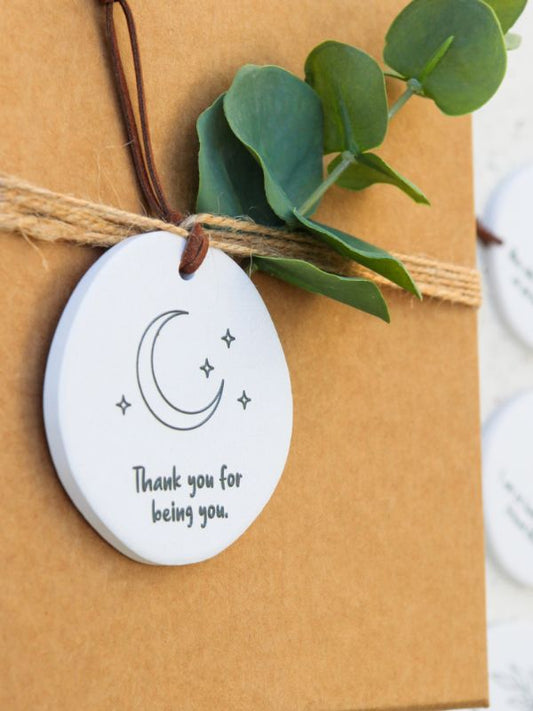 white ceramic decoration with starts and moon, words and some greenery on a brown background