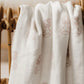 White fabric with embroidered patterns draped over a wooden basket.