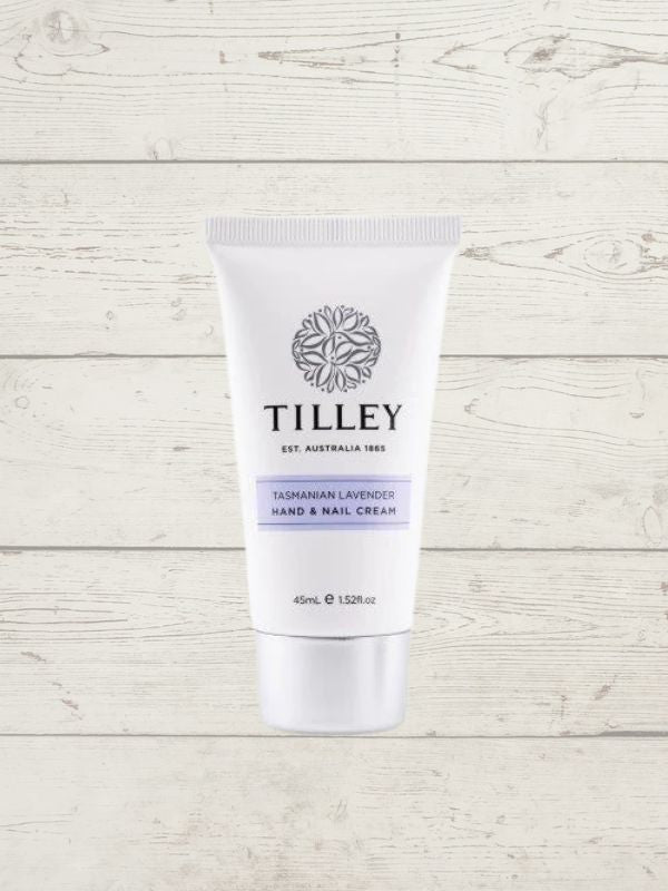 A tube of Tilley Hand Cream against a wooden background. The packaging is predominantly white with blue and black text, and an image of a shea tree in the background.