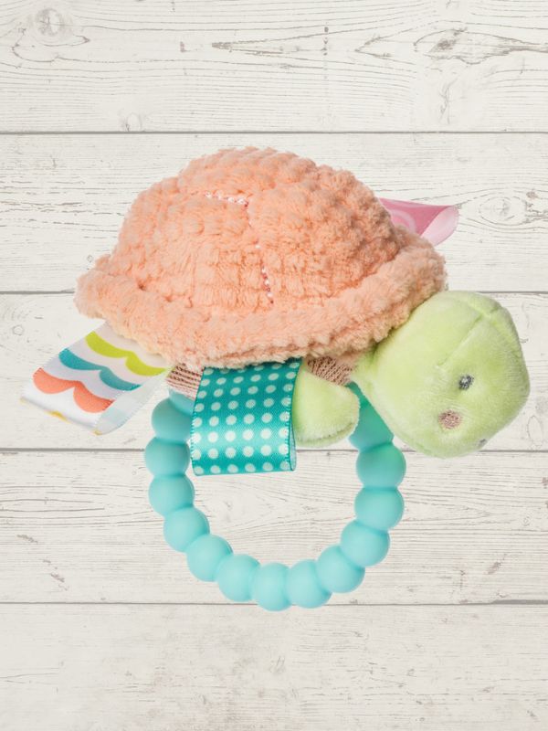 Turtle-shaped teething toy with a soft peach shell and green body on a light wooden surface.