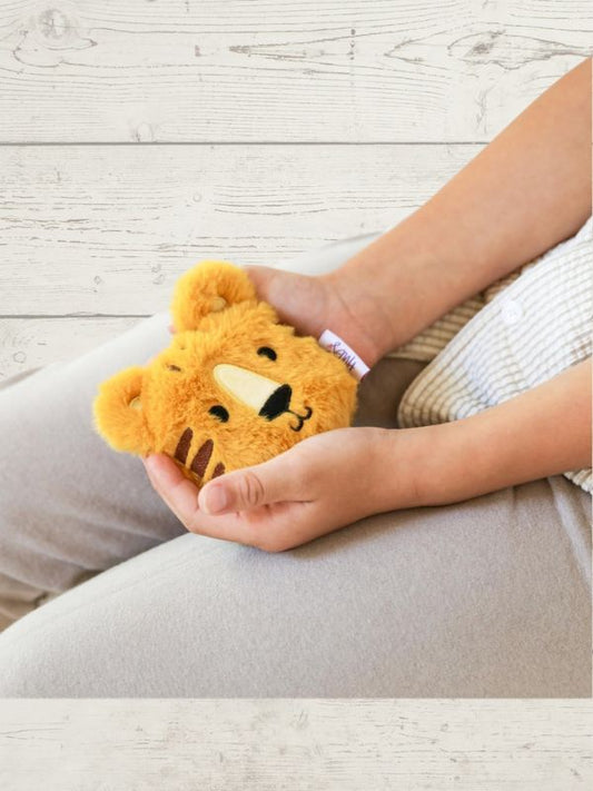 Person holding a small plush toy resembling a bear on a light wooden floor.