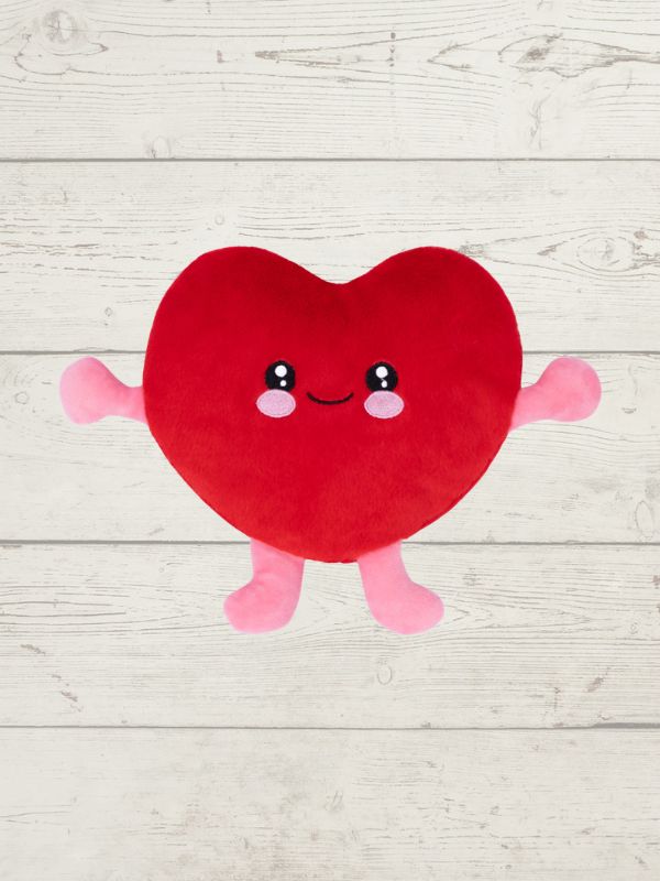 Red heart-shaped plush toy with a smiling face on a light wooden surface