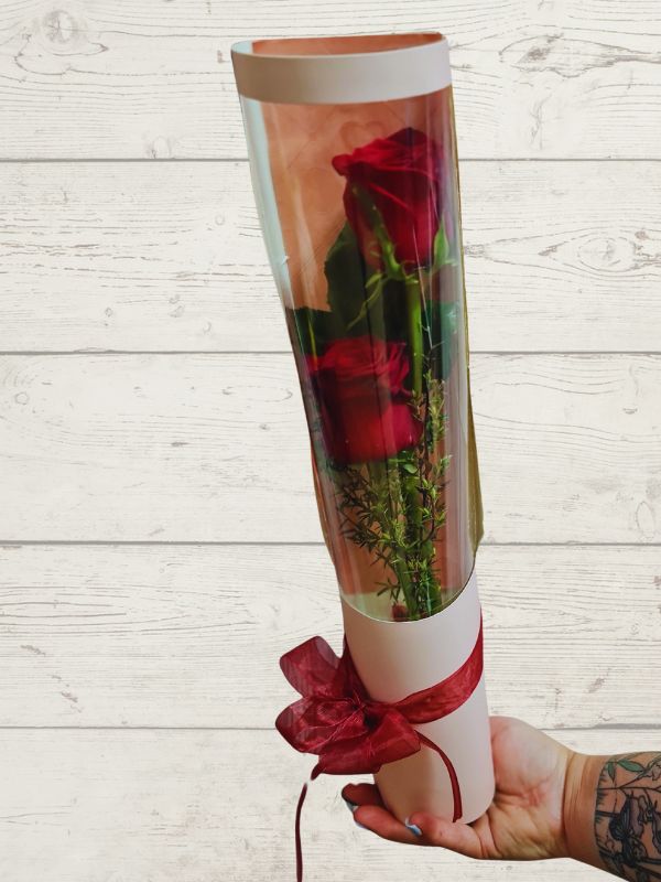 two red roses in pink cylinder with red ribbon
