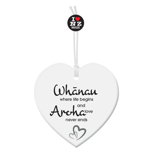 A white heart-shaped hanging memorial plaque with black text reading 'Whânau where life begins and Archa love never ends' and a small heart motif near the bottom. A black circular 'I ❤️ NZ MADE' tag is attached at the top with a white string, shown on a plain white background.