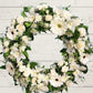 A formal white and green floral sympathy wreath displayed on a wooden background.