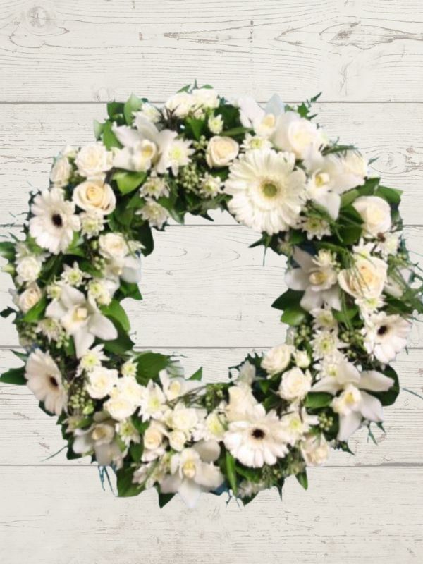 A formal white and green floral sympathy wreath displayed on a wooden background.
