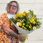 A person holding a yellow and white floral bouquet with wrapping paper.