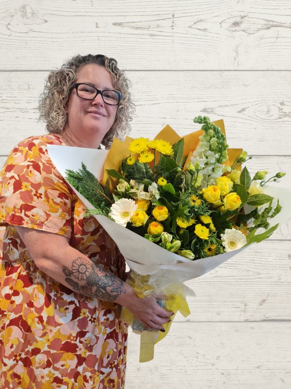 A person holding a yellow and white floral bouquet with wrapping paper.